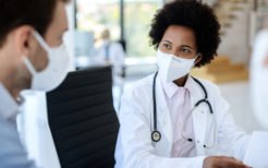 African American doctor wearing protective face mask while talking to a patient at clinic.